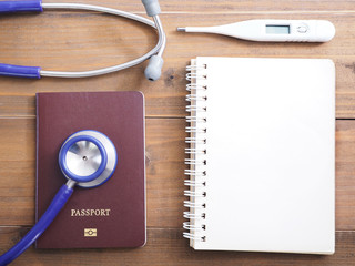 Close up stethoscope, passport, thermometer and blank notepad on wood background