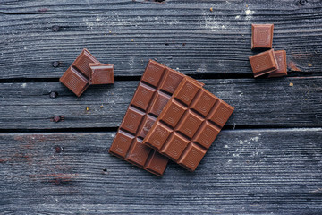 Pieces of a dark chocolate on a grey wooden table.