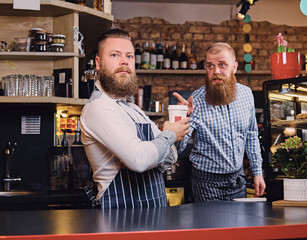 Two bearded hipster coffee shop owners at the counter.