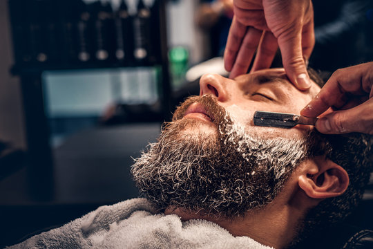 Close up image of barber shaving a man with a sharp steel razor.