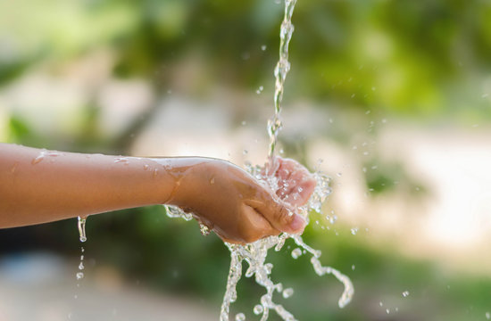 Water pouring in kid hand on nature background, environment issues