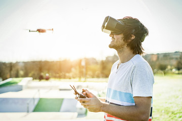 Bearded man using a drone with remote controller wearing virtual reality glasses making photos and videos