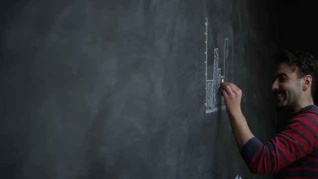  Casual businessman drawing graph on blackboard. Young startup company.