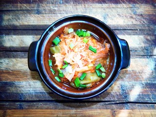 A portion of stewed cabbage with sweet peppers and chopped green onions stands on a brown wooden kitchen board