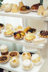 Wedding reception stand with sweets, candies, dessert, cupcakes, muffins, cakes, eclairs decorated with flowers