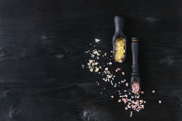 Variety of colorful salt yellow saffron and pink himalayan in wooden spoons over black burnt wood background. Top view with space