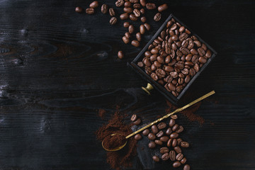 Roasted coffee beans and grind coffee in wood box with spoon over black wooden burnt background. Top view with space.