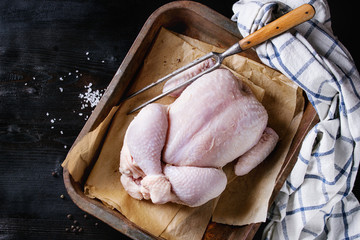 Raw organic uncooked whole chicken with salt and pepper on backing paper in old oven tray with...