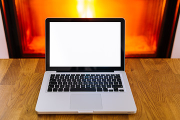 Laptop with blank screen on wooden table in front of burning fireplace