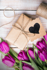 Gift box and tulips bouquet on white wooden background - retro style