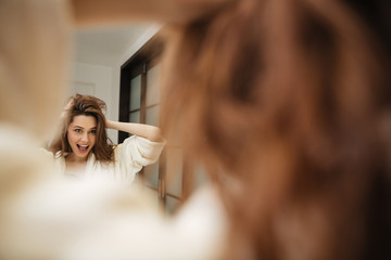 Woman in bathrobe touching hair and having fun at bathroom