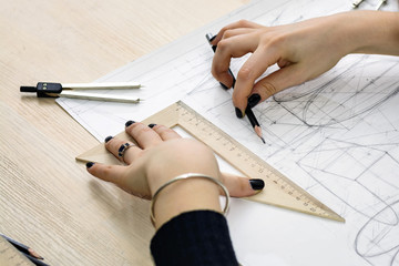 Girl architect draws a plan, design, geometric shapes by pencil on large sheet of paper at office desk.