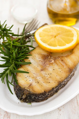 grilled fish with lemon in white dish on wooden background