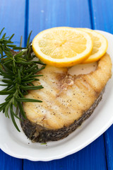 grilled fish with lemon in white dish on wooden background