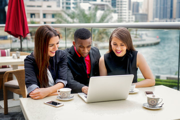 Afro amerian and two caucasian ladies working on laptop outside the office by river.