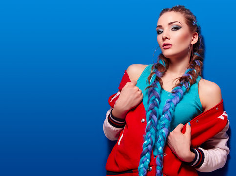 Beautiful young girl with long bright braids. Blue hair, weaving, Bright makeup, red jacket. Cosmetics. Photoshoot on a blue background.