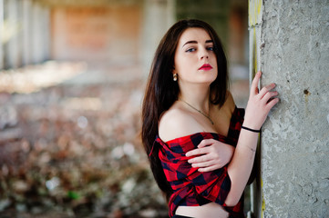 Obraz premium Portrait girl with red lips wearing a red checkered shirt with bare shoulders posed sexy background abadoned place.
