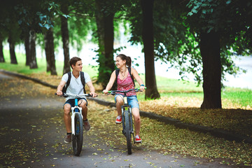 Fototapeta premium Young people, couple with bicycles in the park. A loving couple on a date on a summer evening. The guy with the girl hugs and kisses. Youth, first feelings, first love, first dates