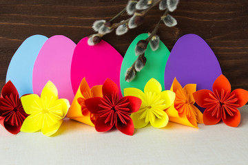 Decorative composition of Easter eggs, paper flowers and willow branches on a wooden background. Selective focus.