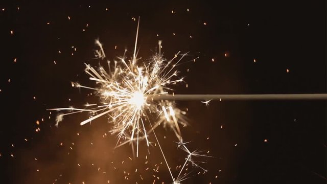 A burning fuse or bengal fire, over a bokeh'd shot of bonfire sparkles floating and flying. Nighttime.
