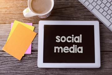 Tablet pc with social media and a cup of coffee on wooden background.