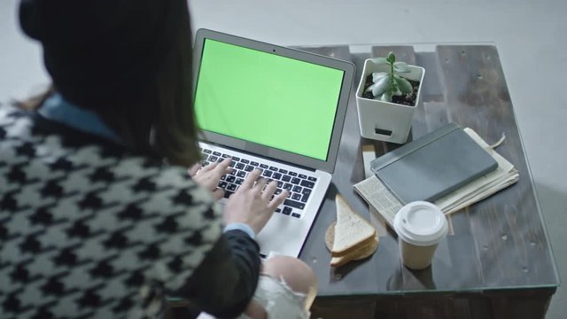 High angle view of woman sitting at table and typing on laptop with green screen 