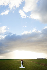 Affectionate young just married couple standing among vast glade covered with green grass