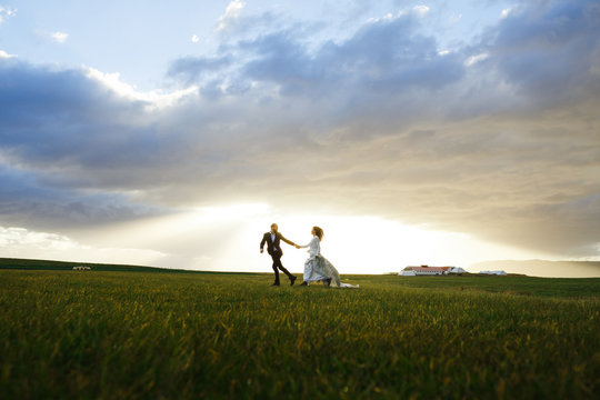 Happy couple running down green meadow in the morning