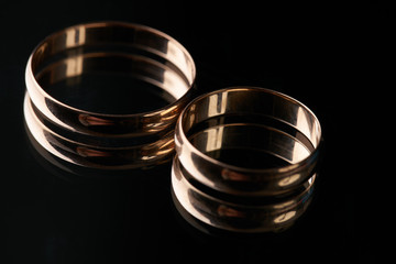 Closeup of Two classical gold wedding rings on isolated black mirror background  on a wedding day. Love and marriage proposal concept.