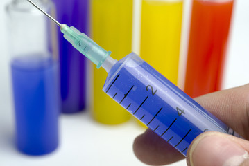 Hand holding test tube with blue liquid and a syringe.