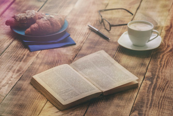 Open old book on wooden table with croissants and coffee