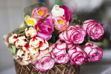 Pink roses and colored tulips are in the basket