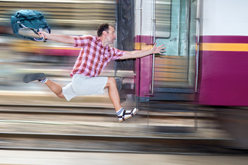 Tourist with bag running behind the train. A man runs for a moving wagon. Backpacker hurries for train departing from the station. Journey to the last minute.
