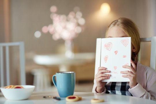 Shy girl hiding her face behind paper card with drawn red hearts