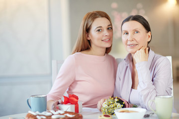 Young and mature females sitting by table and celebrating holiday