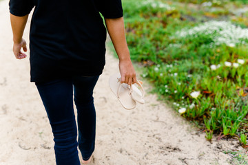 Frau barfuß mit Flipflops in der Hand auf einem Weg