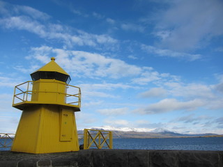 Fototapeta na wymiar Bright yellow lighthouse by the sea in Reykjavik, Iceland