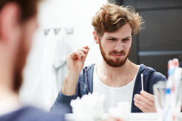 Young man looking at cotton-bud while cleaning his ears