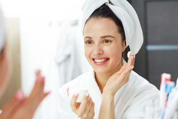 Smiling girl with towel on head going to apply face cream