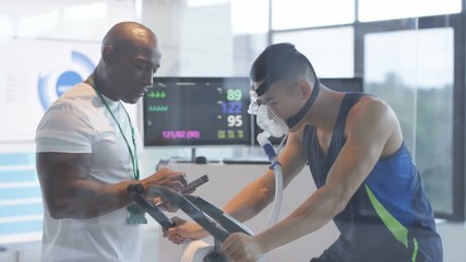 Sports professional analyzing man's fitness levels with hi tech equipment. Professional athlete in training, personal trainer at the gym or scientific research concept. 