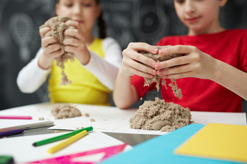 Creative girls making figures from kinetic sand at lesson