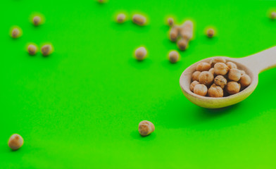 Fototapeta na wymiar gold chickpeas in wooden spoon on green background , tasty vegan food, top view