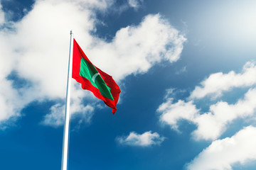 National flag of Republic of Maldives at blue cloudy sky