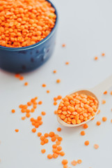 Red lentil in bowl and wooden spoon on white background
