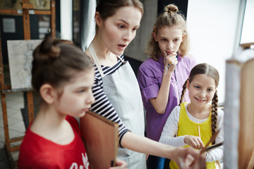 Group of kids looking at easel while their tutor commenting sketch