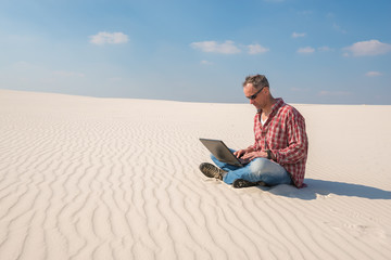 Fototapeta na wymiar Concerned man with a laptop sits in desert
