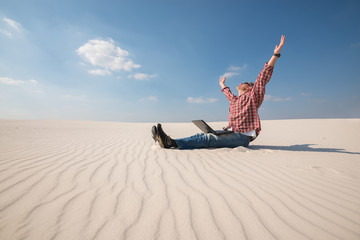 Man with a laptop sits in the middle of the desert