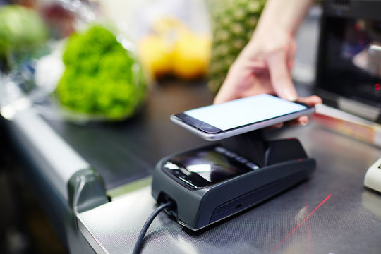 Modern consumer keeping smartphone over cashier-machine to pay for purchase in supermarket