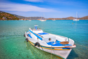 Wooden fishing boat and yachts anchored at the tropical waters of the famous gulf of Elounda, the village of celebrities, near Spinalonga, Crete, Greece.