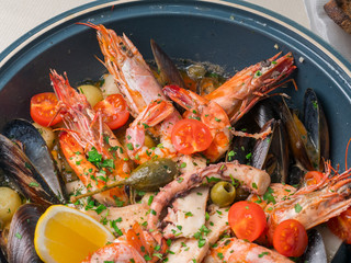 Colorful fresh seafood with vegetables and spices on blue plate in restaurant